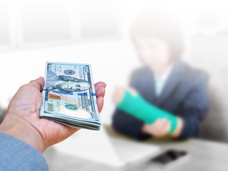 hand holding American dollar currency isolated on blurred blackground injured woman with broken hand and green cast on arm, insurance health concept.