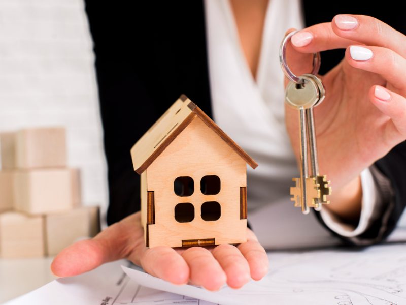 woman-holding-set-keys-with-wooden-house